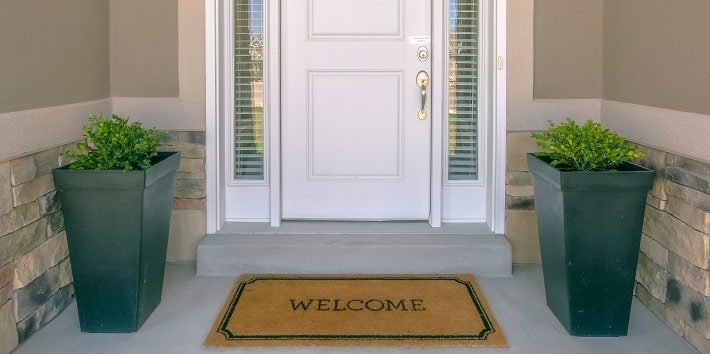 玄関外に“WELCOME”の玄関マットがひかれており、両端に観葉植物が置かれている様子。